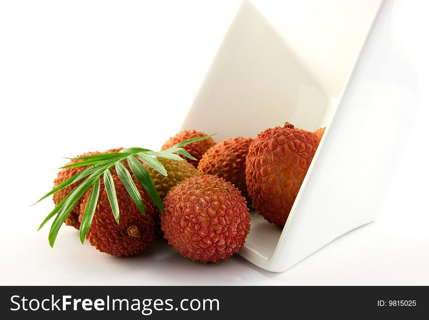 Lychee and green leaf spilling out a dish with clipping on a white background. Lychee and green leaf spilling out a dish with clipping on a white background