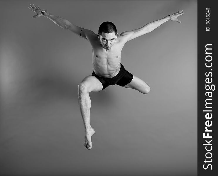 Young muscular dancer leaping over gray background