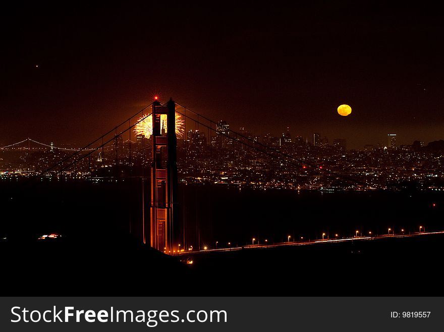 San Francisco Golden Gate Bridge At Night with Fireworks and a Full Moon showing the Transamerica Building through the bridge. San Francisco Golden Gate Bridge At Night with Fireworks and a Full Moon showing the Transamerica Building through the bridge