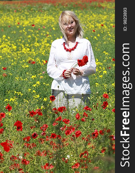 The blonde on the meadow assembles red poppies. The blonde on the meadow assembles red poppies