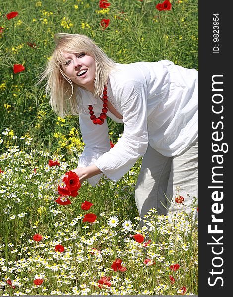 The blonde assembles flowers on the meadow. The blonde assembles flowers on the meadow