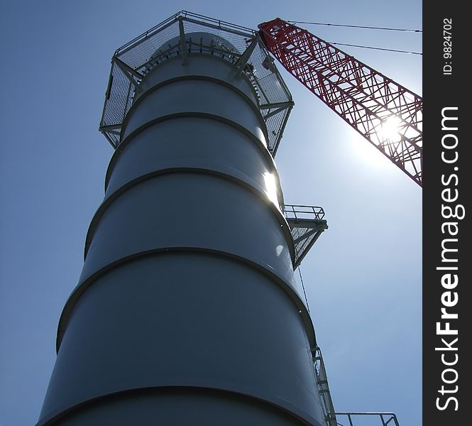 Smoke stack with crane through sun