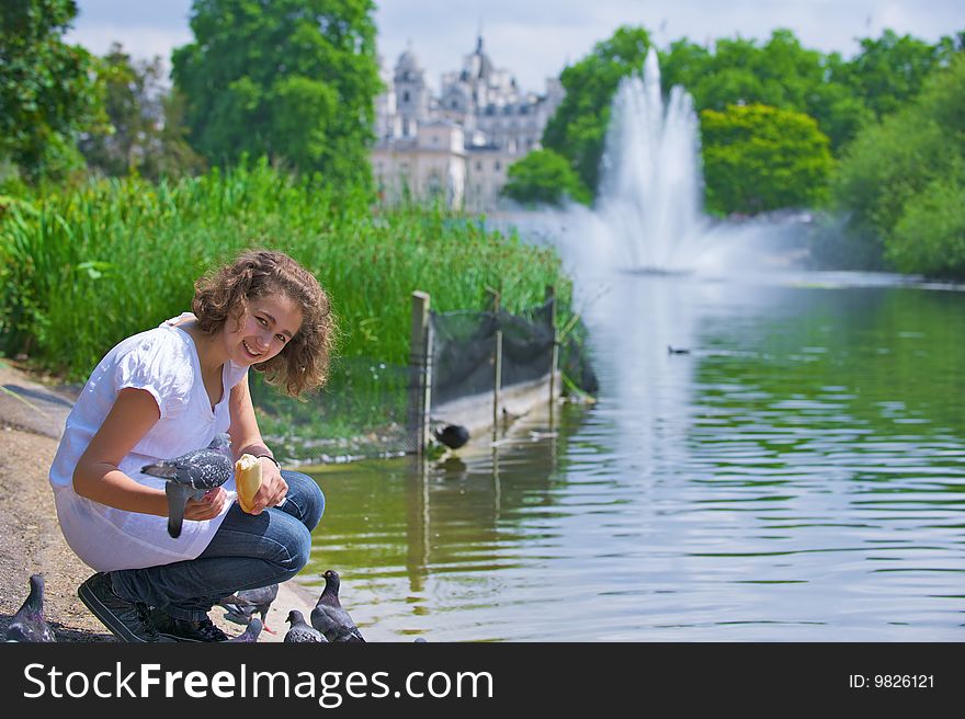 The girl with curly hair sits near water and feeds birds. The girl with curly hair sits near water and feeds birds