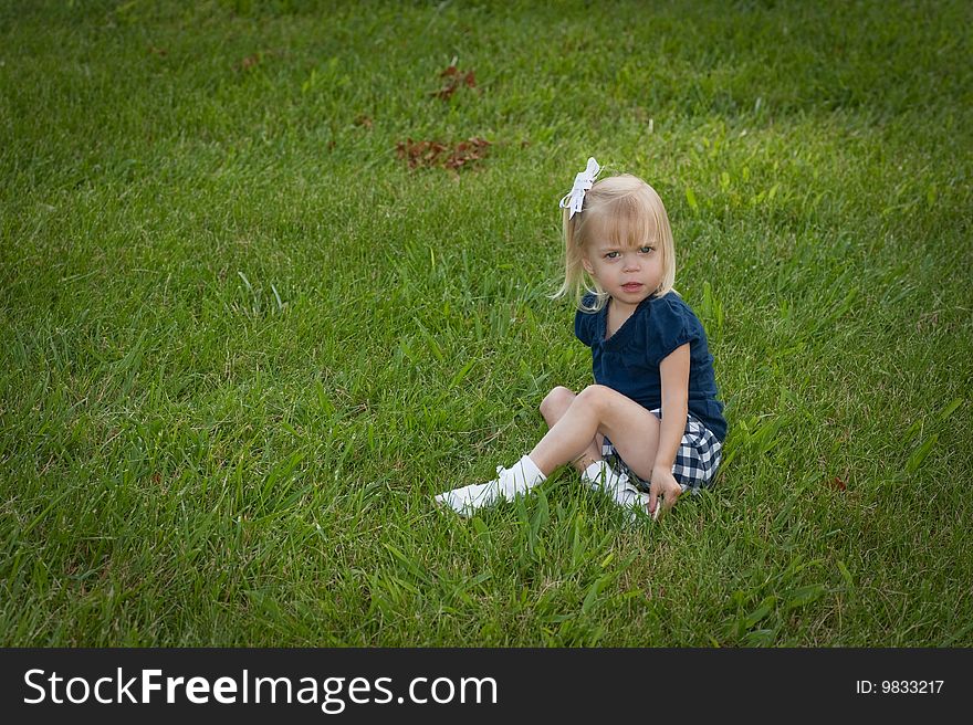 Little girl sitting in the grass looking at the camera she is all alone. Little girl sitting in the grass looking at the camera she is all alone