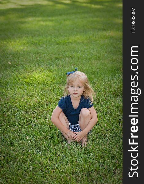 Little girl sitting in the grass looking down at the ground with a sad look on her face, she is all alone. Little girl sitting in the grass looking down at the ground with a sad look on her face, she is all alone
