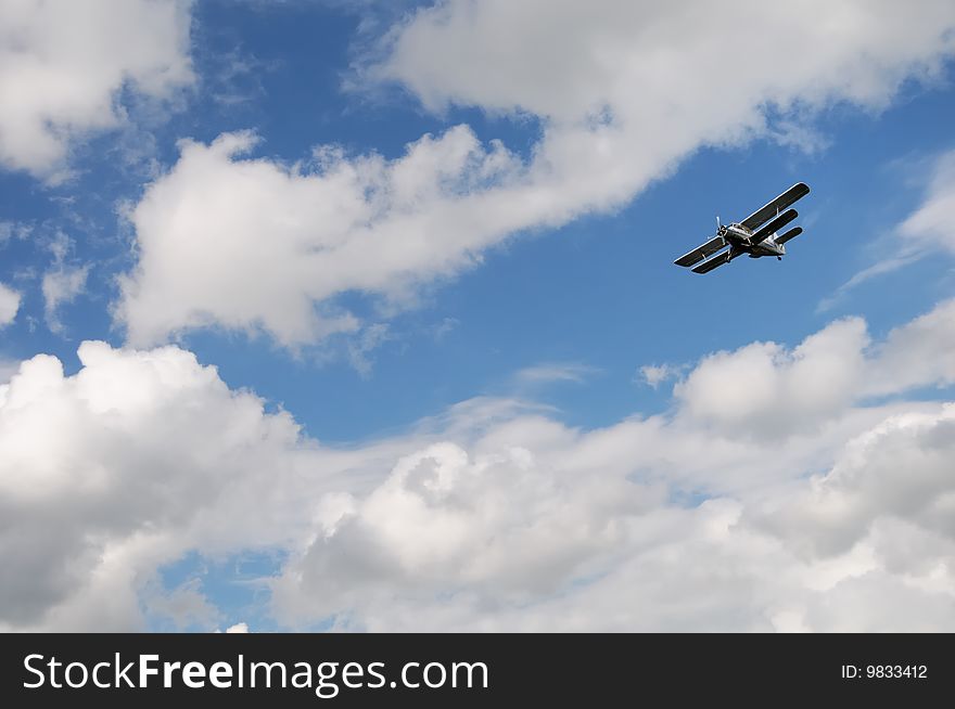 An airplane flying in the blue sky with cumulus clouds. An airplane flying in the blue sky with cumulus clouds