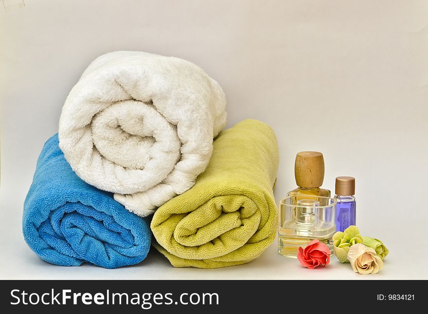 Colorful towels stacked on each other beside bottles of perfumes and lotions and among flowers. Colorful towels stacked on each other beside bottles of perfumes and lotions and among flowers