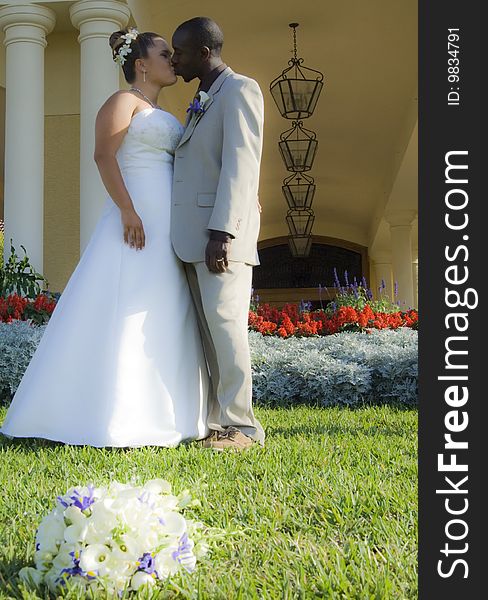 A bride and groom kissing in front of country club with bouquet of flowers in grass. A bride and groom kissing in front of country club with bouquet of flowers in grass.