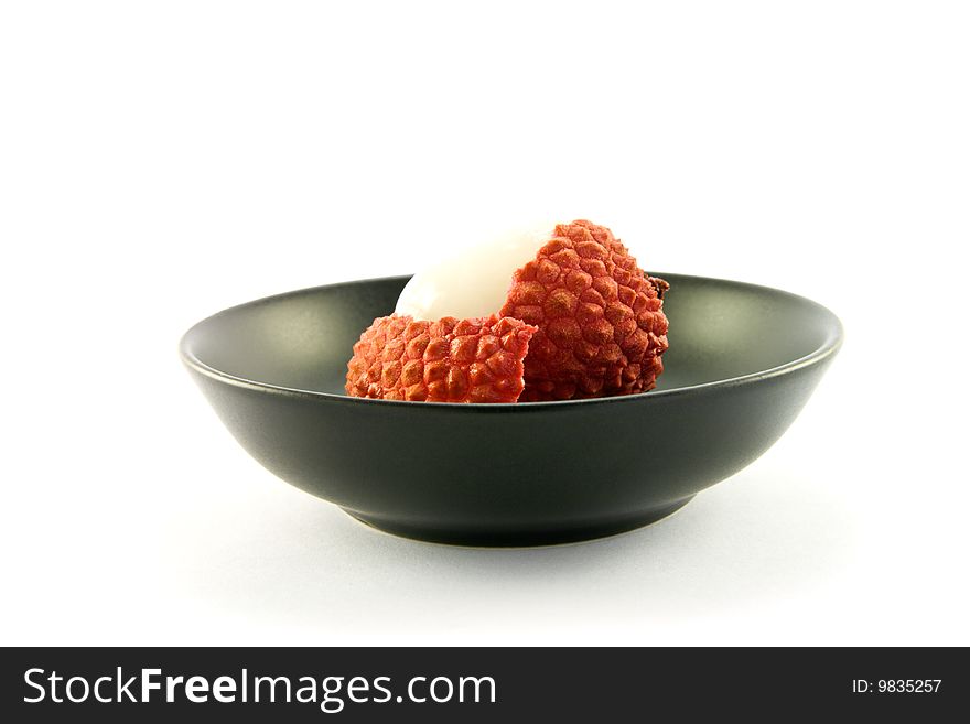 Single peeled lychee in a black dish with clipping on a white background