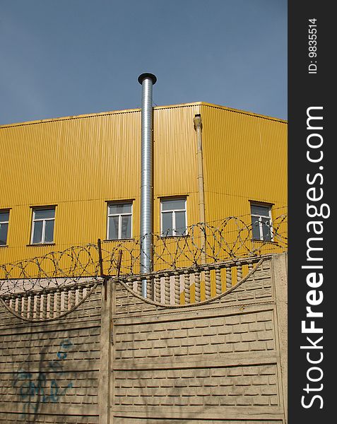 A secured industrial zone with concrete fence and barbed wire on the blue sky background.