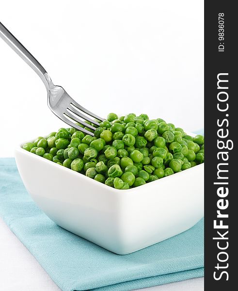 Bowl of green peas with a fork coming in from the left. White background. Bowl of green peas with a fork coming in from the left. White background