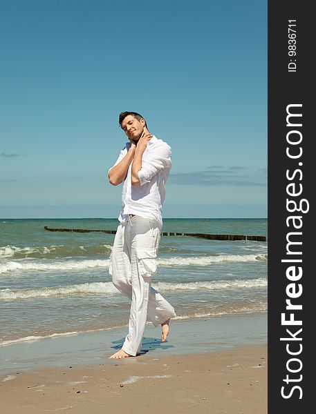 Man walking down the coast feeling carefree and free . relaxing with hands on head . little waves in background. Man walking down the coast feeling carefree and free . relaxing with hands on head . little waves in background