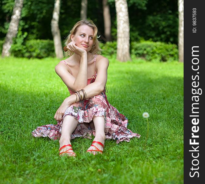 Girl sits on a lawn, supports her face by hand and looks sideways. Girl sits on a lawn, supports her face by hand and looks sideways