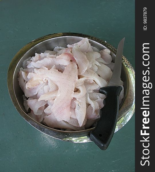 A stainless steel bowl filled with crappie fillets & fillet knife