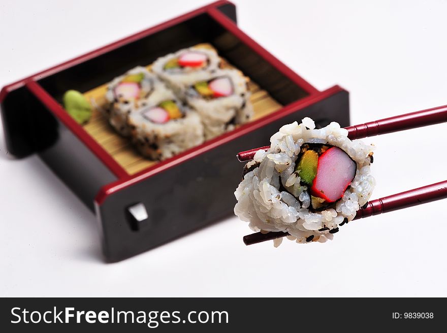 California sushi rolls in a box being handled with a chopstick.