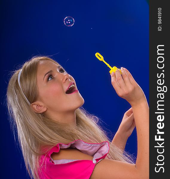 Young beautiful blond inflate soap bubbles on a blue background