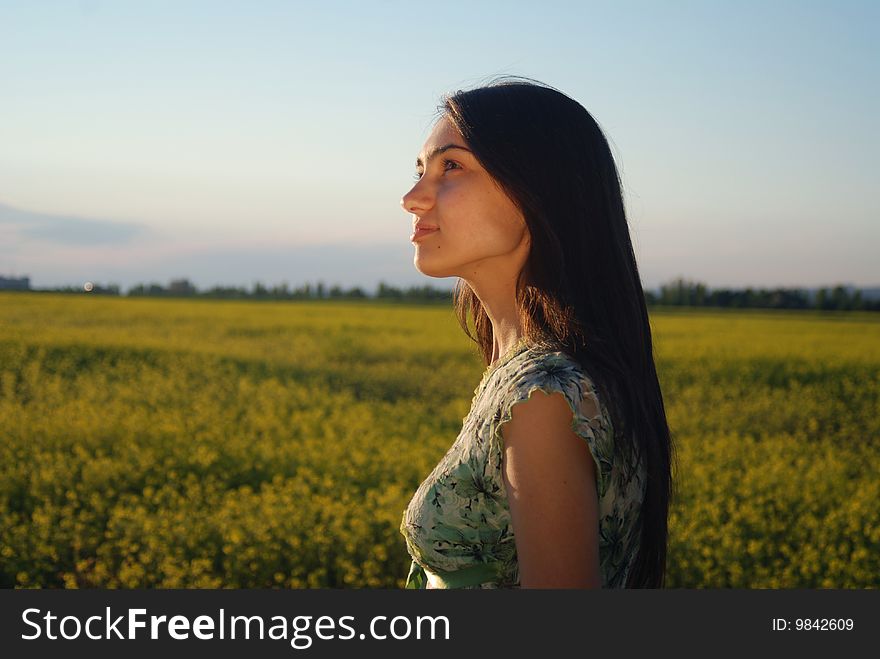 A beautiful girl standing on a field with yellow canola. A beautiful girl standing on a field with yellow canola