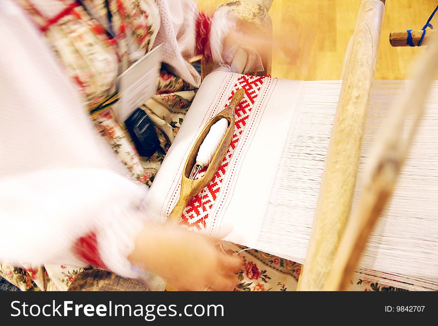 Woman dressed in folk clothing weaves a towel with a shuttle at the ancient Russian wooden loom at a folk festival. Woman dressed in folk clothing weaves a towel with a shuttle at the ancient Russian wooden loom at a folk festival