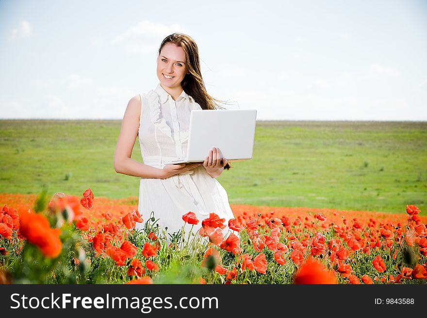 Smiling beautiful girl with laptop in the poppy field