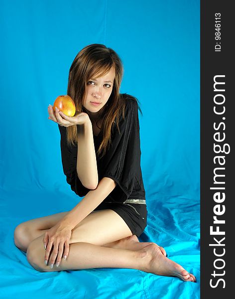 Girl holds in the hand apple survey in the studio against the blue
background. Girl holds in the hand apple survey in the studio against the blue
background