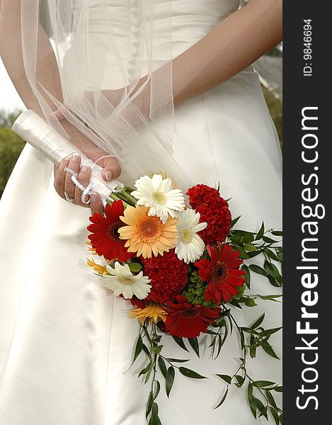 A bride waits holding her bouquet behind her back. A bride waits holding her bouquet behind her back