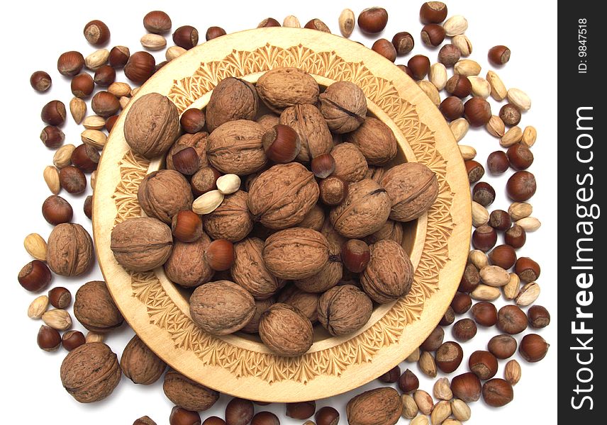 Walnuts, pistachioes, hazelnuts in a wooden plate on a white background.