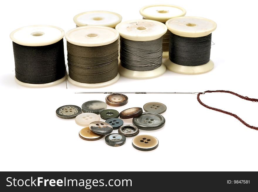 Thread spindles, buttons and needle isolated on white background.