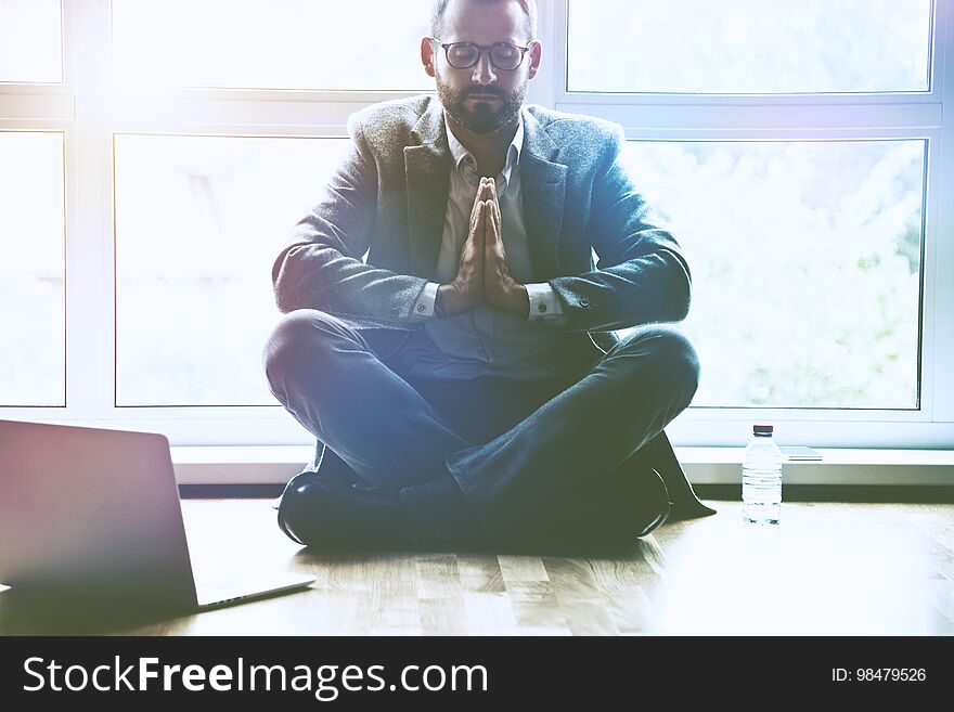 Businessman doing yoga in lotus pose at office workplace with laptop