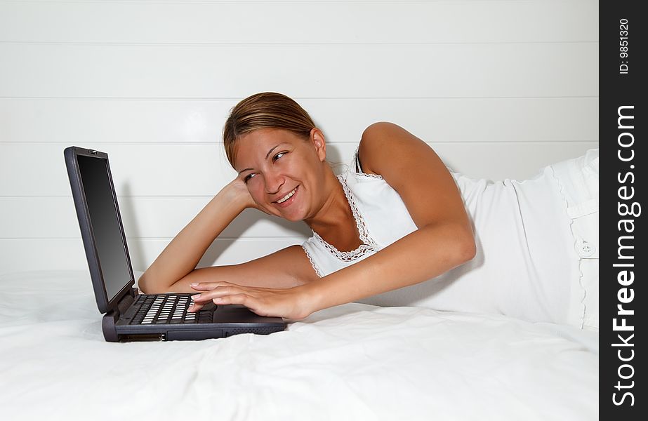 Pretty young woman laying down on bed and working at computer. Pretty young woman laying down on bed and working at computer