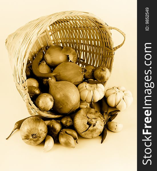 Still life of a onions, garlic and chilies tumbling from a rattan basket, in golden tones