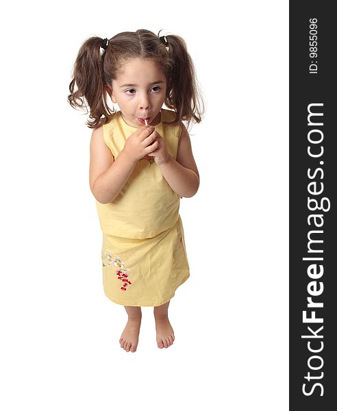 A small preschool girl eating a sweet lollipop. She is barefoot and wearing a skirt and top with hair in ponytails. A small preschool girl eating a sweet lollipop. She is barefoot and wearing a skirt and top with hair in ponytails.