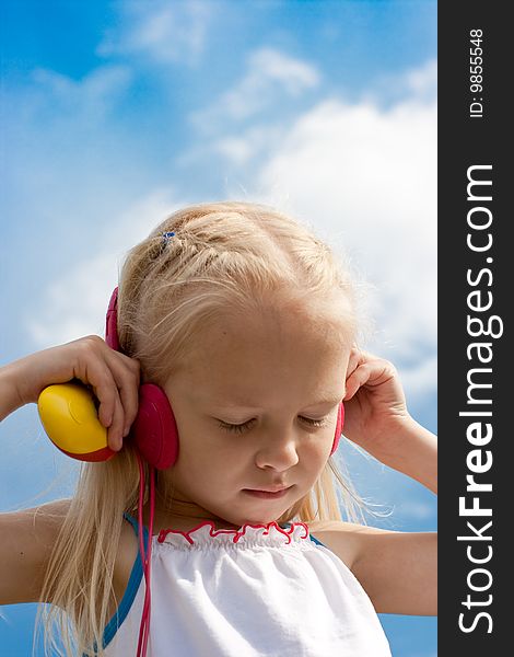 Little blonde girl with closed eyes in red earphones listens mp3 player music outdoor. Little blonde girl with closed eyes in red earphones listens mp3 player music outdoor