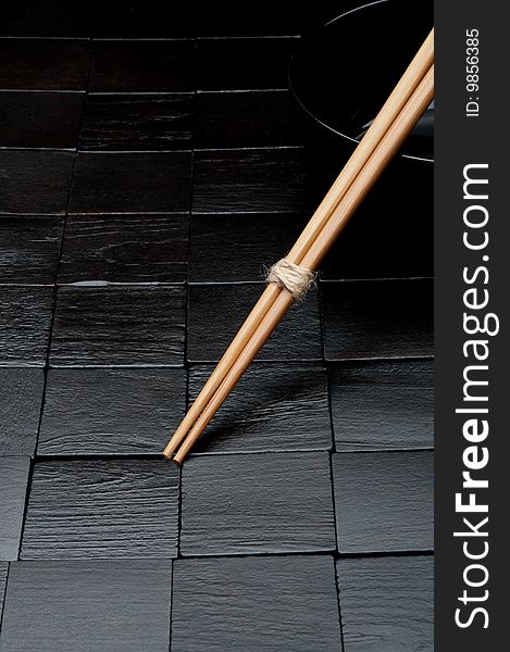 Chopsticks resting on a black bowl on a black wood background