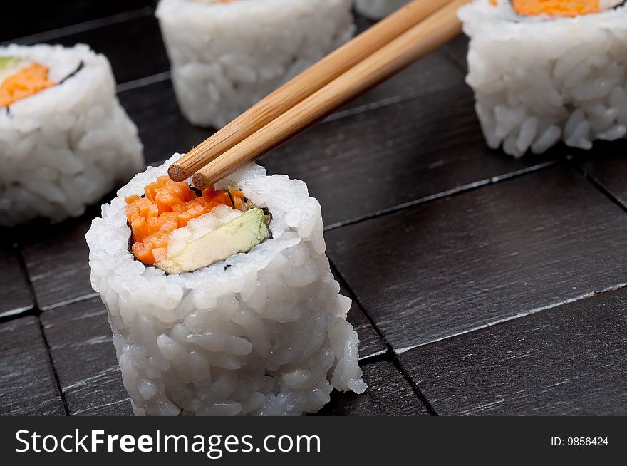 A tilted horizontal shallow focus macro of sushi with chopsticks on a black wooden background. A tilted horizontal shallow focus macro of sushi with chopsticks on a black wooden background