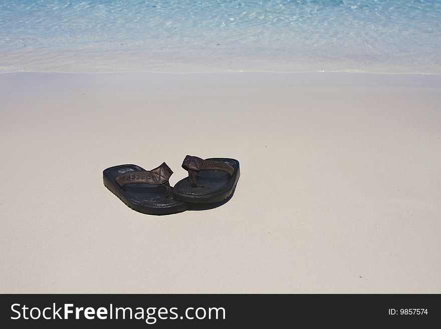 A pair of flip-flops or sandals on a white sand beach. A pair of flip-flops or sandals on a white sand beach