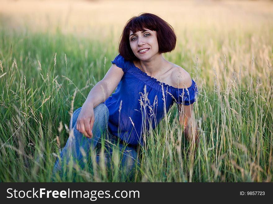 The smiling woman sits in a grass