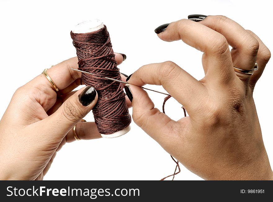 Female hand holding thread spindle and needle.