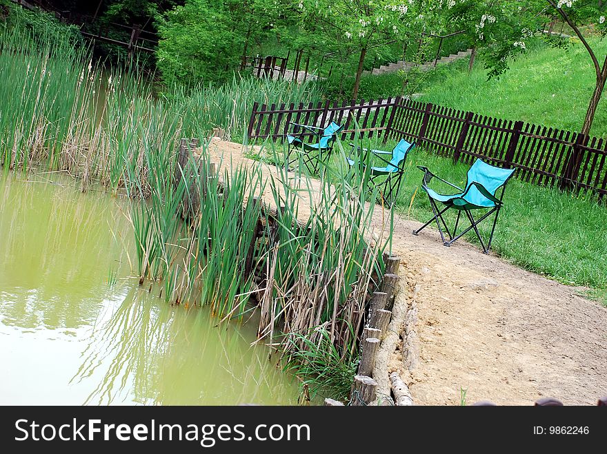 Folding blue chairs by muddy yellowish pond. Folding blue chairs by muddy yellowish pond