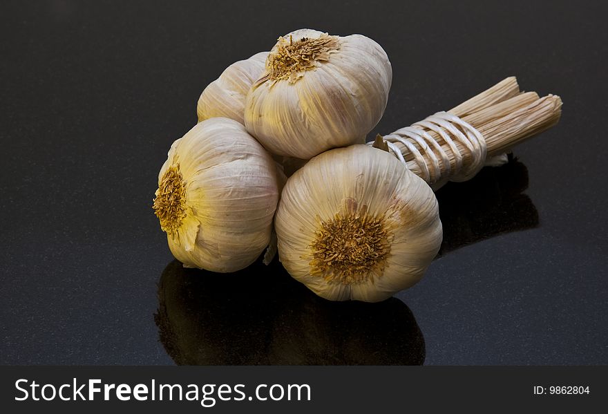 Three Bulbs of Garlic tied together on black marble work surface