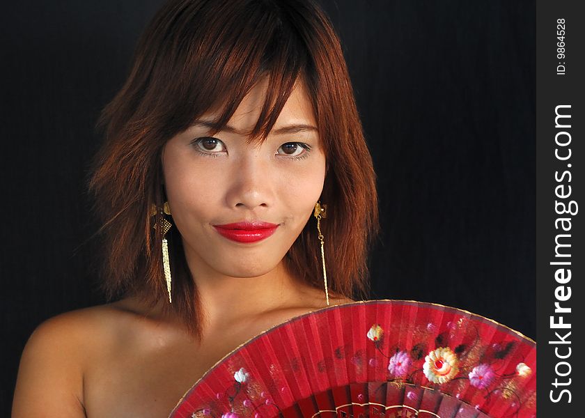 Very seductive young asian woman with a fan on a black background