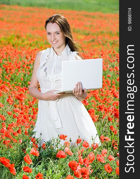 Smiling beautiful girl with laptop in the poppy field