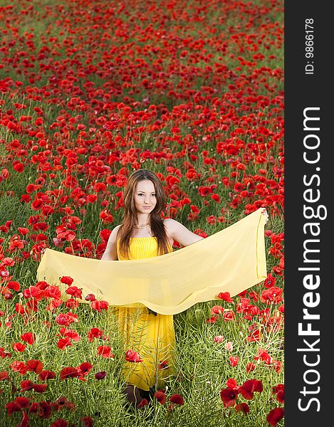 Beautiful young girl with yellow scarf in the poppy field, high angle view