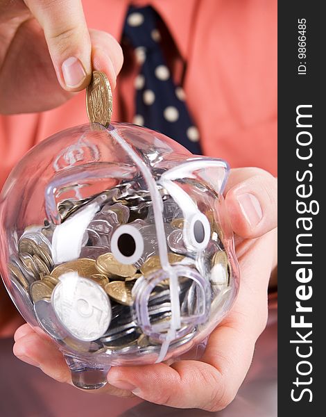 Businessman inserting coin into transparent piggy bank