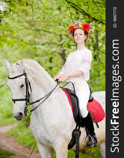 Beautiful girl in floral wreath riding horse