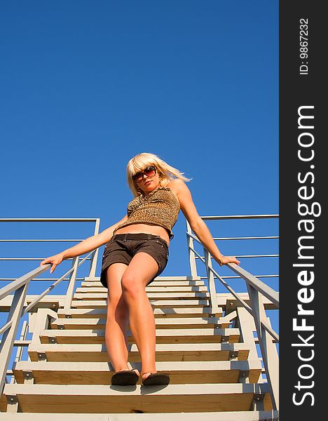 The blonde the Girl is beautiful stands on a ladder leaving in the bright blue sky. The blonde the Girl is beautiful stands on a ladder leaving in the bright blue sky