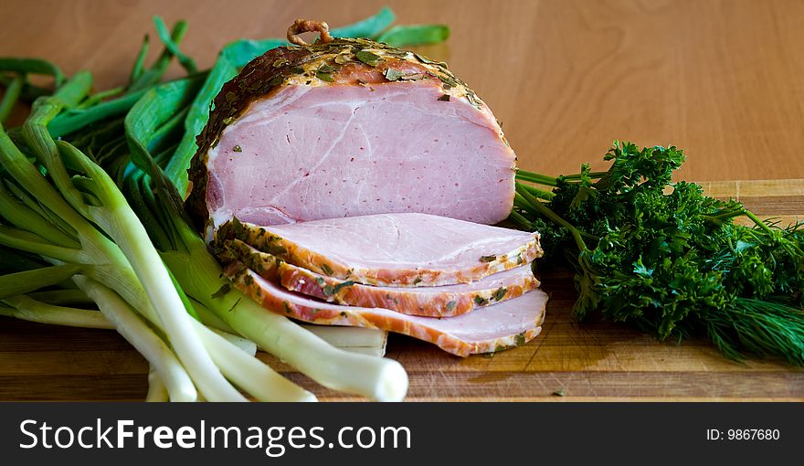 Appetizing slices of ham with potherbs on the kitchen table. Appetizing slices of ham with potherbs on the kitchen table