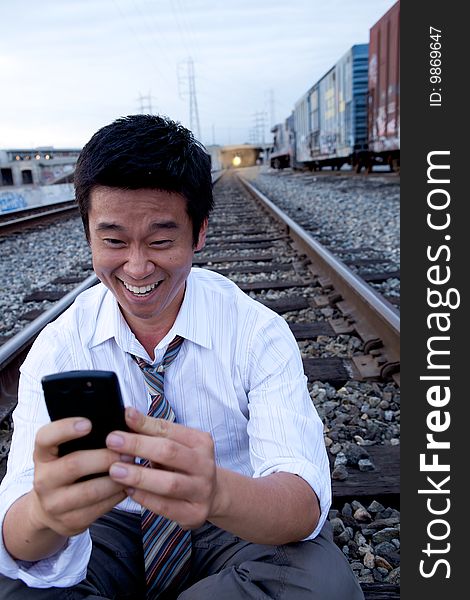 An Asian man sitting on the train tracks making a call. An Asian man sitting on the train tracks making a call