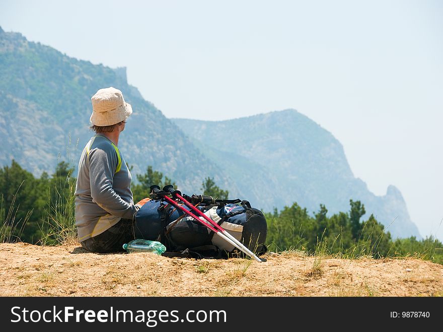 Tired hiker relaxes on a hill and enjoys landscape