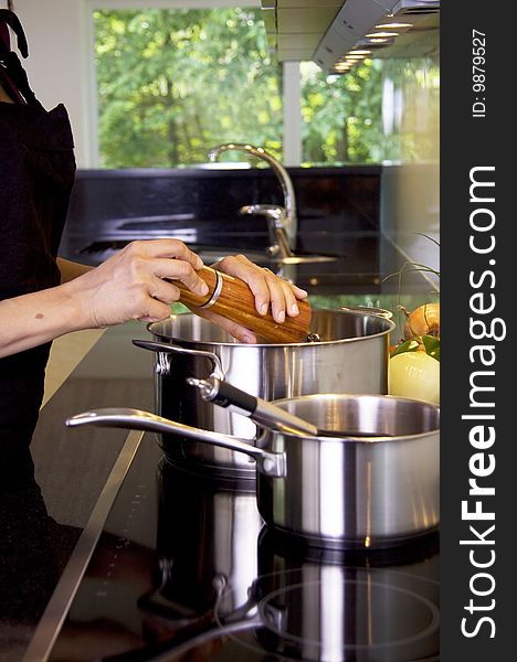 A woman is cooking in a modern kitchen and adding pepper in the saucepan. A woman is cooking in a modern kitchen and adding pepper in the saucepan