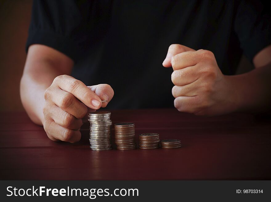 man put money on pile of coins on wood table